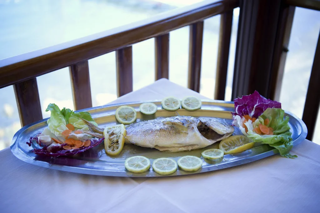 Pesce al forno con limone servito in terrazza, con il mare sullo sfondo