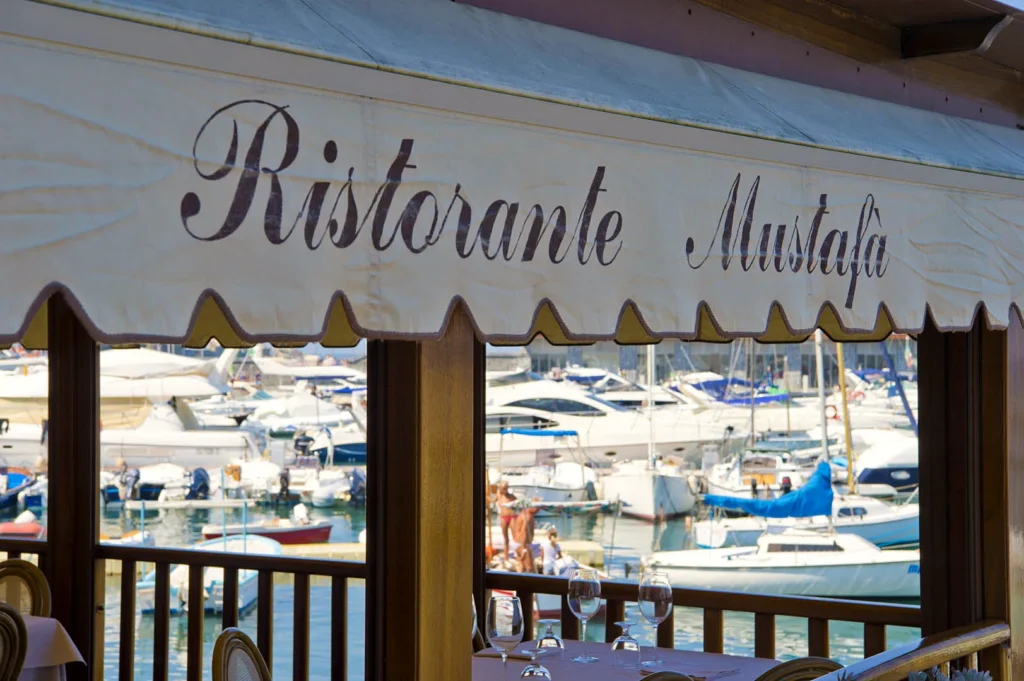 La tenda con l’insegna Ristorante Mustafà e le barche nel porticciolo